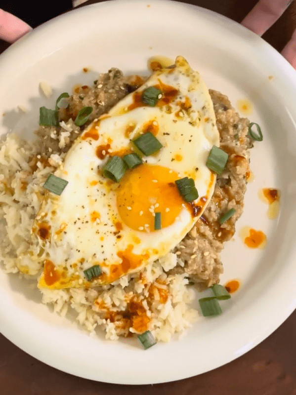 hearts of palm white rice topped with soy savory oatmeal, a fried egg with a runny yolk, and scallions