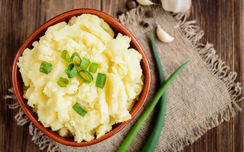 Mashed potatoes in bowl on wooden table with spring green onion and garlic