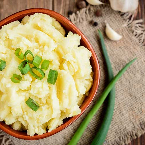 Mashed potatoes in bowl on wooden table with spring green onion and garlic